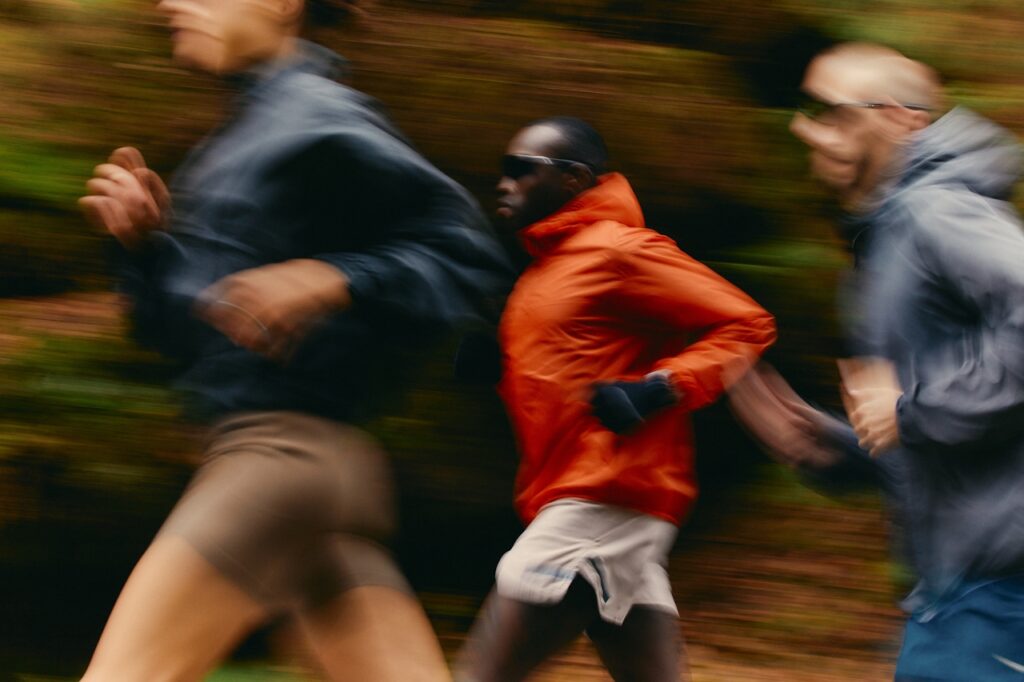 Runners in motion on a trail, one wearing an orange jacket